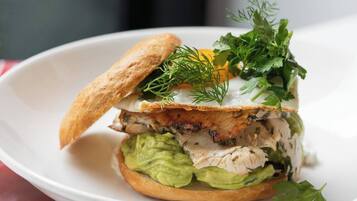 Un sándwich con aguacate, pollo y un huevo escalfado sobre un plato blanco.