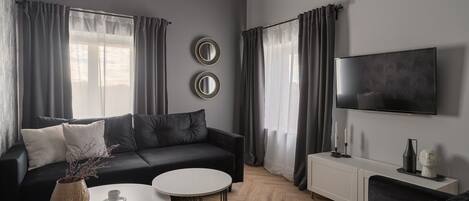 Een moderne woonkamer met een zwarte bank, twee witte salontafels, een televisie en een minimalistische inrichting.