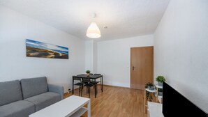 Un salon moderne comprenant un canapé, une table à manger avec des chaises, une table basse blanche, un téléviseur et une porte.
