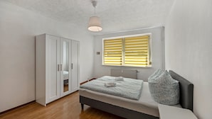 Une chambre à coucher comprenant un lit, une armoire, un radiateur et une fenêtre avec des stores.