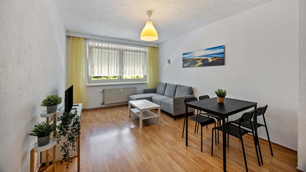Un salon moderne comprenant un canapé, une table à manger et des chaises, un téléviseur et une fenêtre avec des stores.