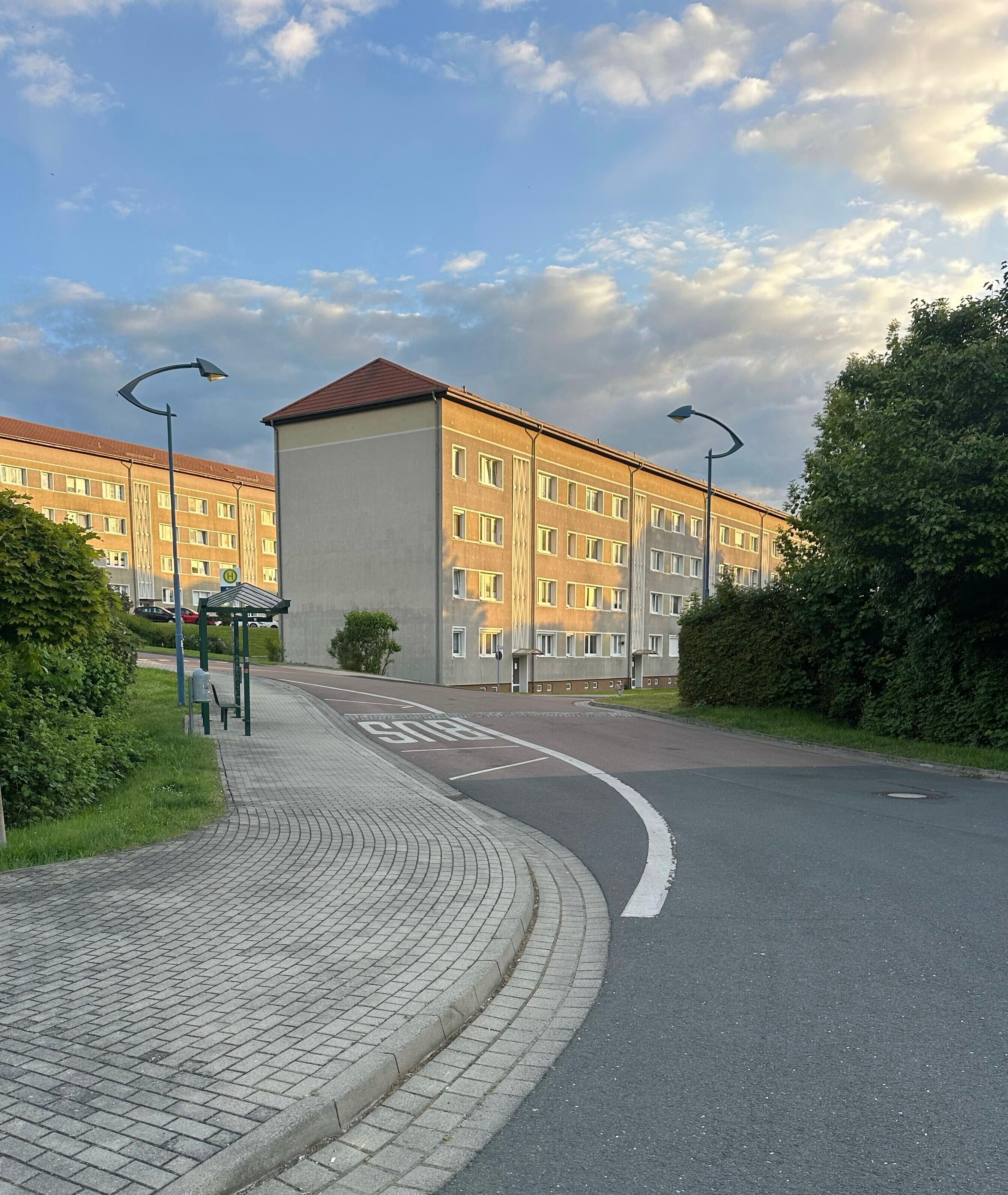 Un immeuble à plusieurs étages, doté d’un toit plat, d’une allée pavée et d’une route qui tourne vers la droite.