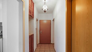 Un couloir avec une porte en bois, un luminaire au plafond et un sol carrelé.