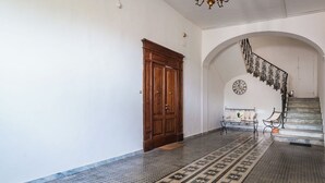 Un couloir avec une porte en bois, un sol à motifs, un escalier avec une rampe en fer forgé et une horloge murale.