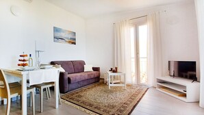 Un soggiorno con divano, televisore, tavolo da pranzo, sedie e un quadro appeso al muro.