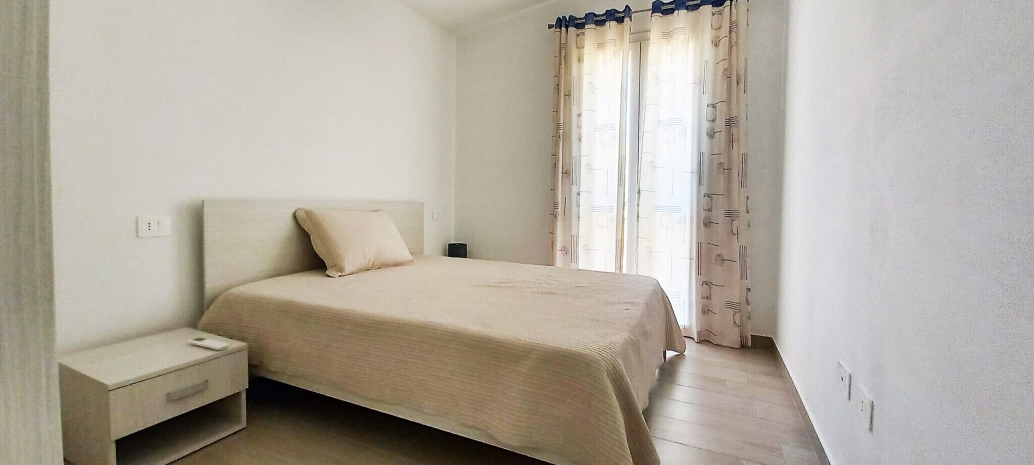 Un dormitorio con cama, mesita de noche y cortinas.