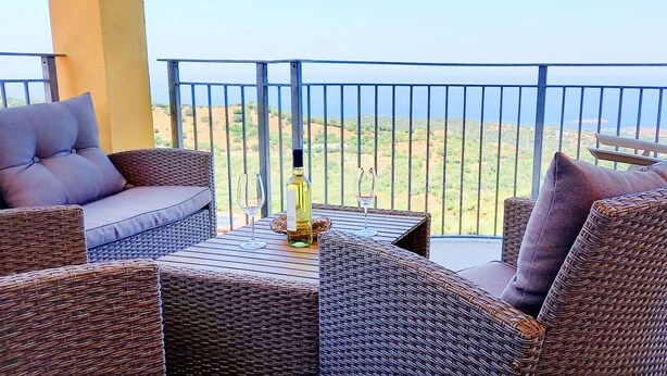Un balcone con mobili in vimini, un tavolo con una bottiglia e un bicchiere, e vista sul paesaggio.