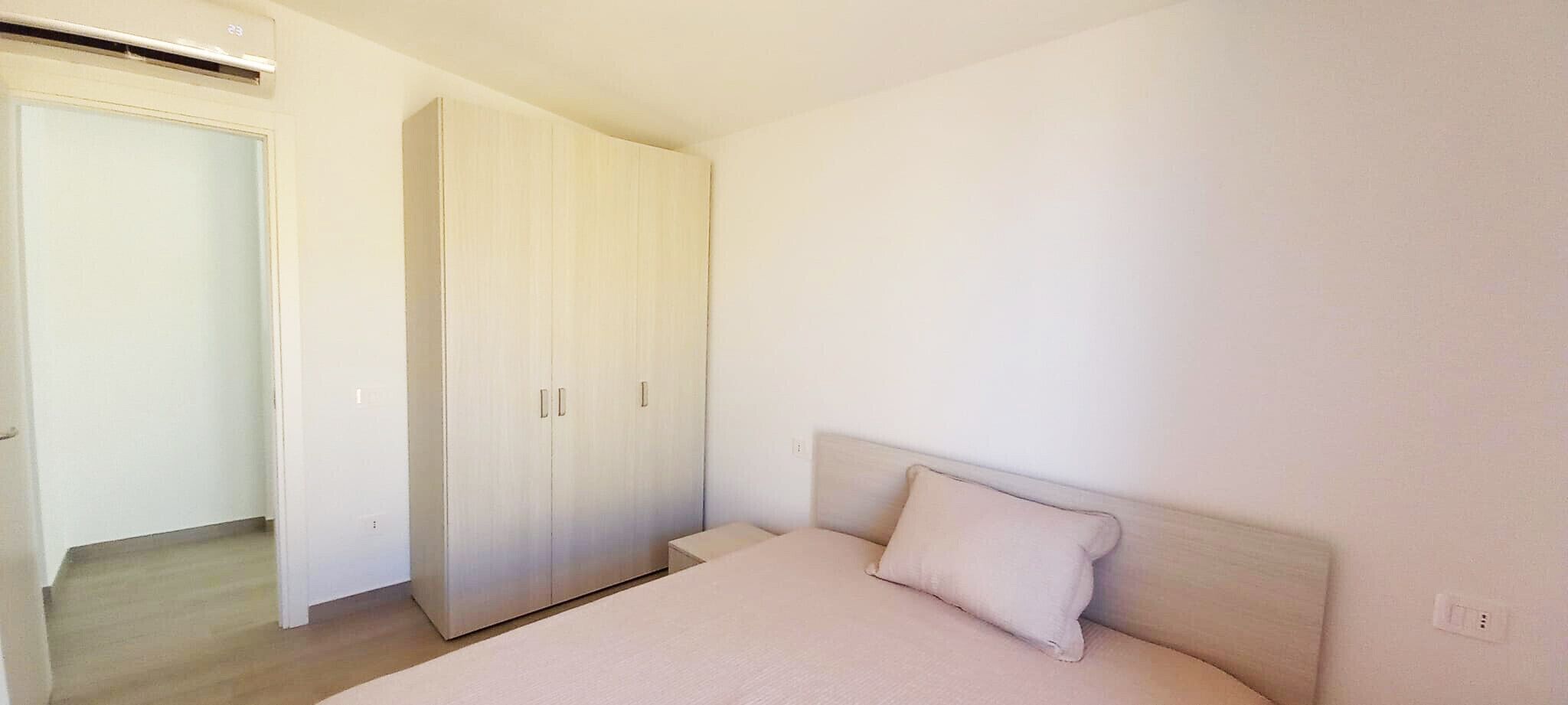 Een slaapkamer met een bed, een kledingkast en een deur naar een andere kamer.