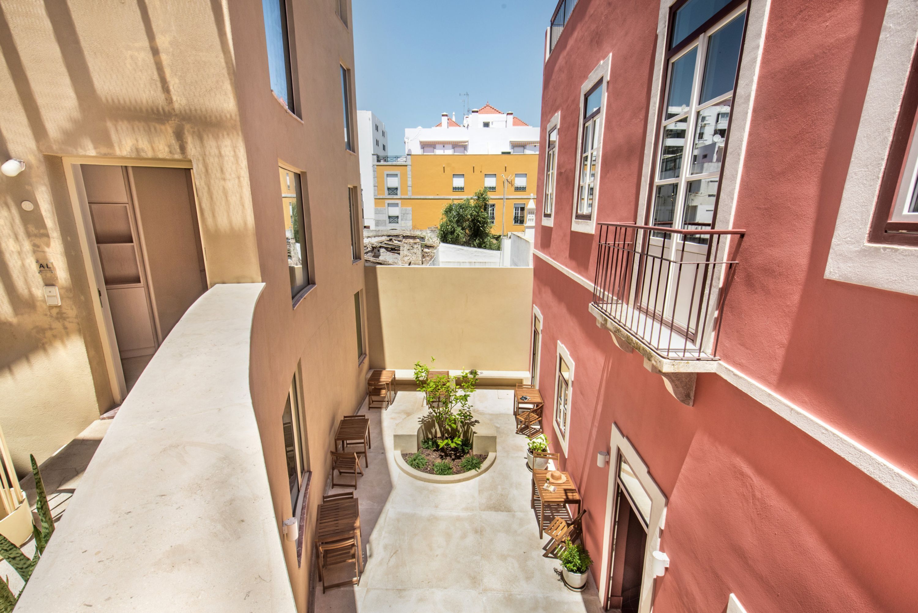 Un estrecho callejón con un pequeño patio, bancos de madera y plantas en macetas.