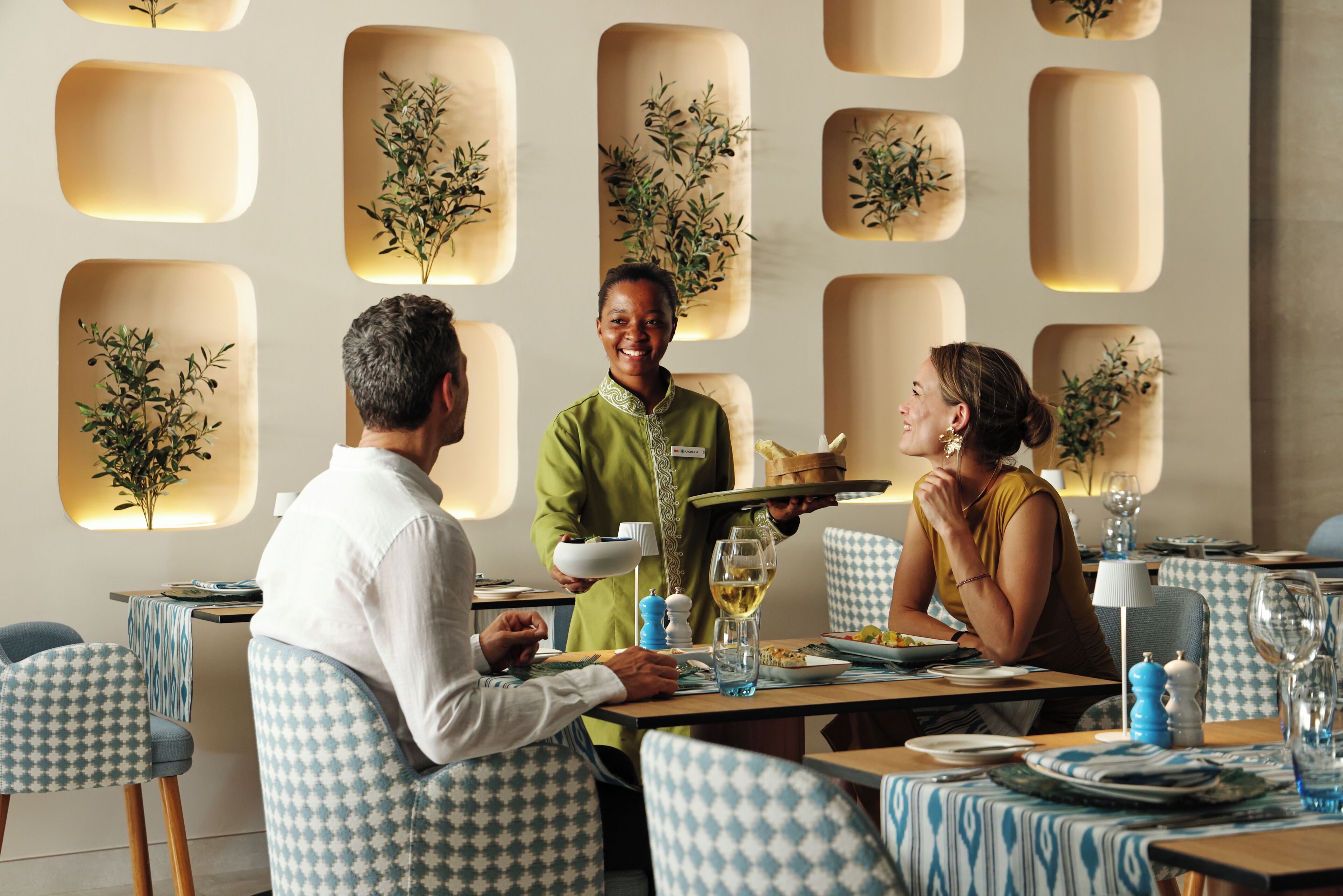 A restaurant with checkered chairs, a waiter serving, and a table with wine glasses.