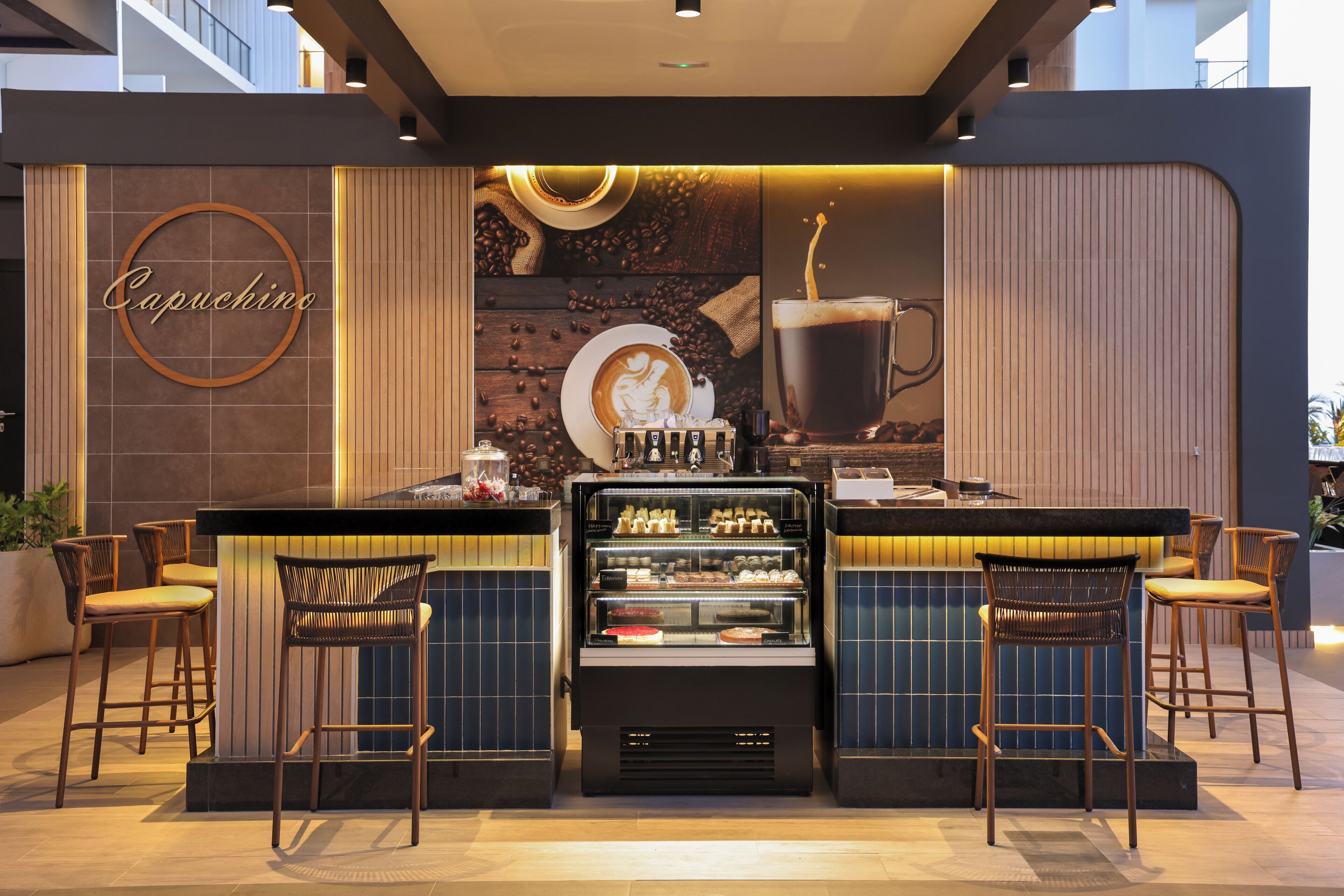 Un café doté d’une machine à café, d’une vitrine réfrigérée et de tabourets de bar.