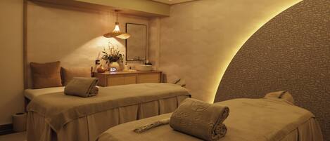 A spa room with two beds, a mirror, a sink, and a wall with a textured pattern.