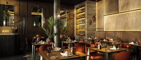 Un restaurante con mesas dispuestas para comer, una zona de bar y una pared decorativa con textura.