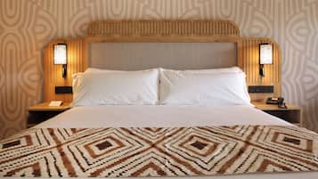 A hotel room with a large bed, two bedside tables with lamps, and patterned wallpaper.
