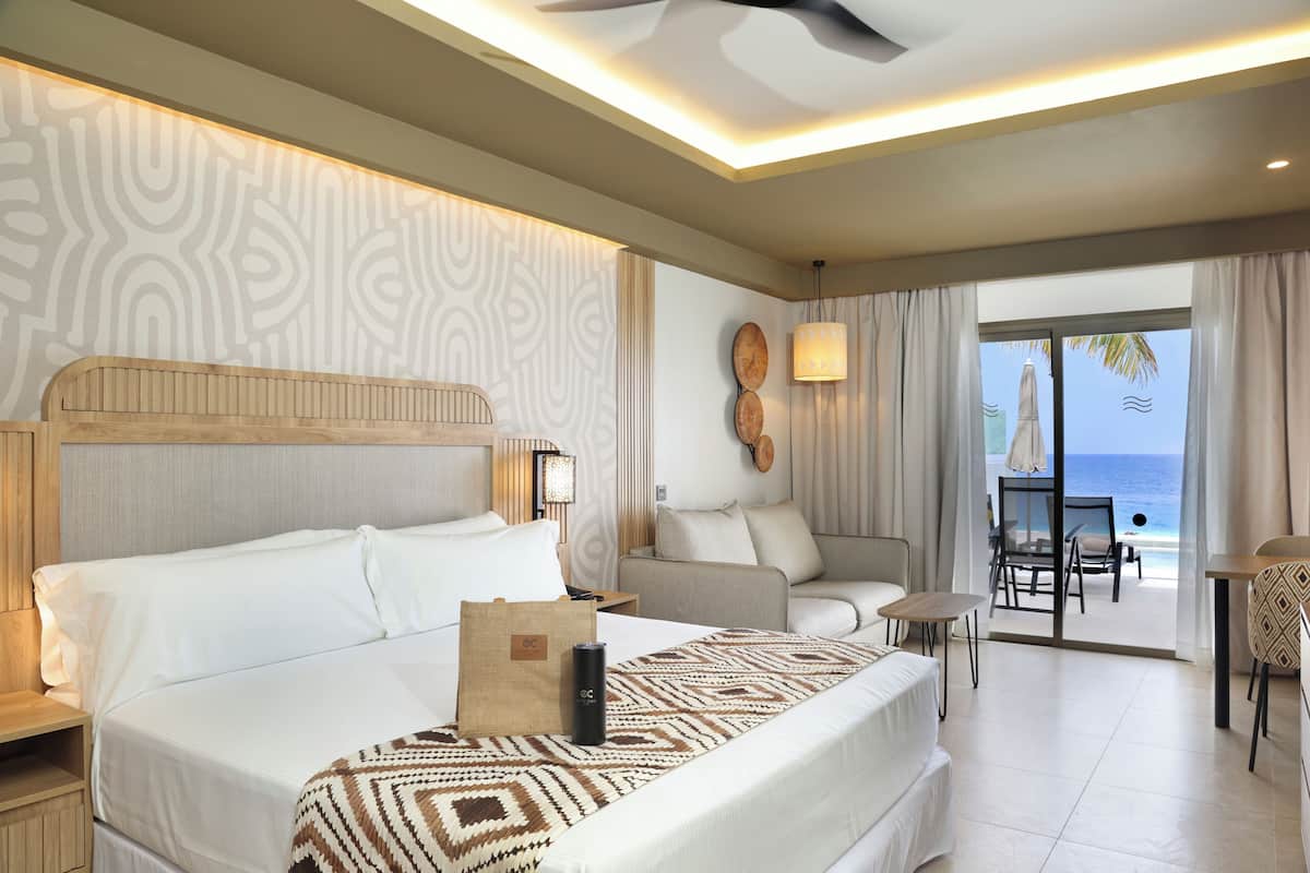 A hotel room with a bed, a sofa, a table, and a view of the ocean.
