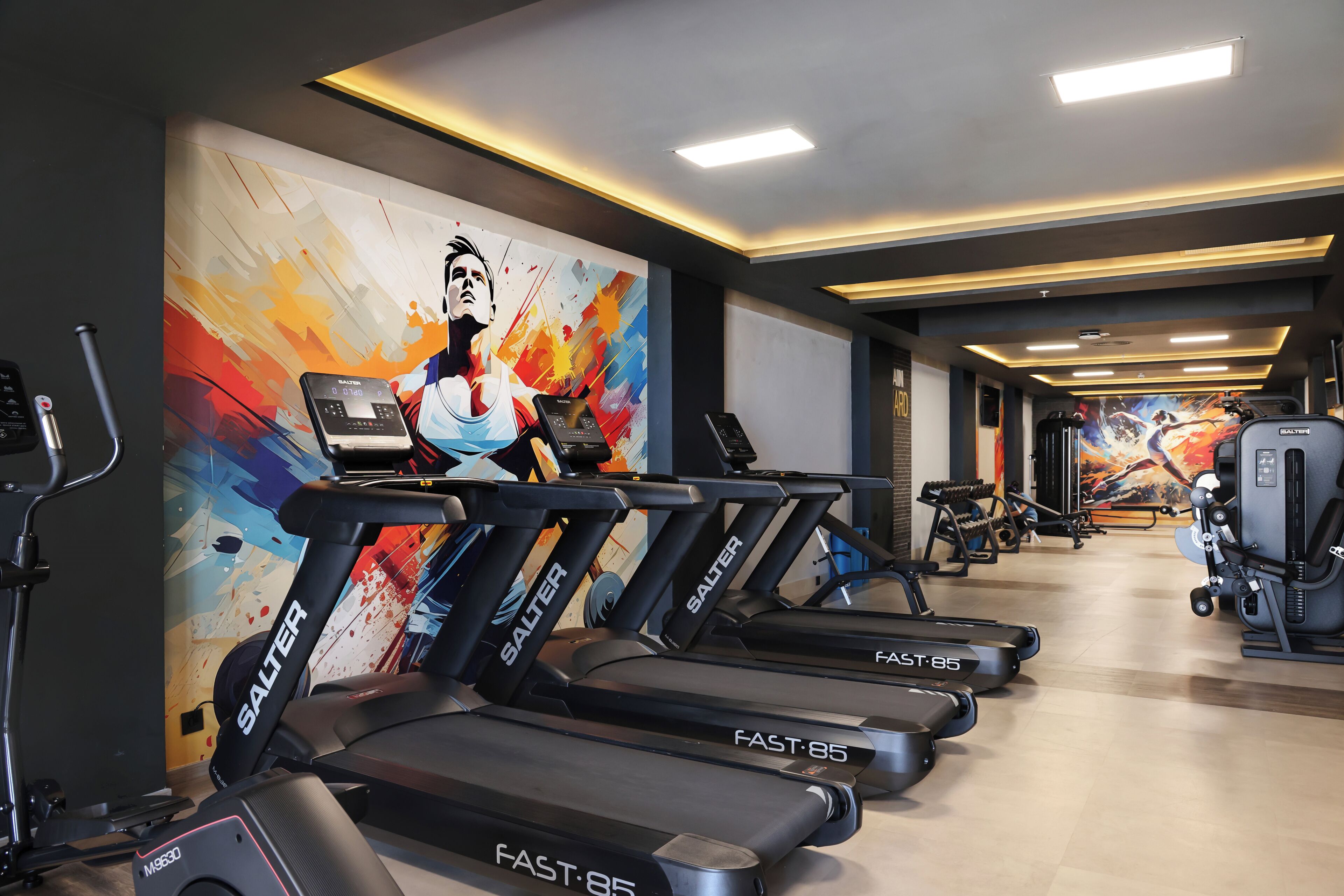 A gym with multiple treadmills, weight machines, and a colorful mural on the wall.
