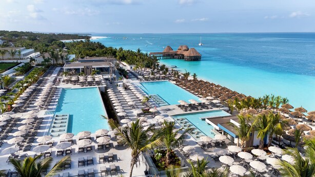 Un resort con varias piscinas, camas sol, sombrillas y bungalows sobre el agua.
