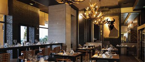 A restaurant with multiple tables set for dining, a chandelier, and a mounted animal head on the wall.