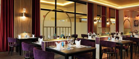 A restaurant with tables set for dining, purple chairs, and a modern interior design.