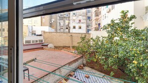 A view from a window overlooking a courtyard with a brick floor, a small tree with green leaves, and a building with multiple windows and balconies in the background. - Bright and Spacious 2-Bedroom Apartment Steps from Florida Metro (Red Line). (L'Hospitalet de Llobregat)