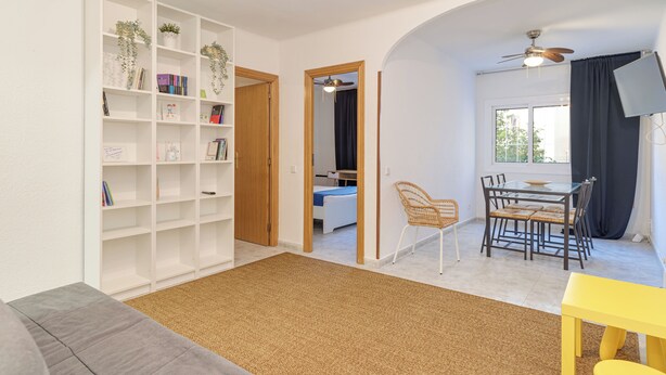 A living room with a bookshelf, a dining table with chairs, a sofa, and a ceiling fan. - Bright and Spacious 2-Bedroom Apartment Steps from Florida Metro (Red Line). (L'Hospitalet de Llobregat)