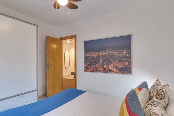 Un dormitorio con vista a la ciudad, una cama con almohadas de colores, una puerta de madera y un ventilador de techo.