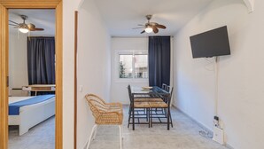A room with a bed, a dining table with chairs, a ceiling fan, a TV mounted on the wall, and a window with curtains. - Bright and Spacious 2-Bedroom Apartment Steps from Florida Metro (Red Line). (L'Hospitalet de Llobregat)