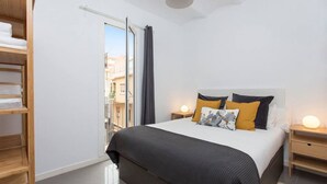 Un dormitorio con cama, mesitas de noche, armario y ventana con cortinas.