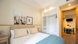 A bedroom with a large bed, a wardrobe, a TV, and a dining area.