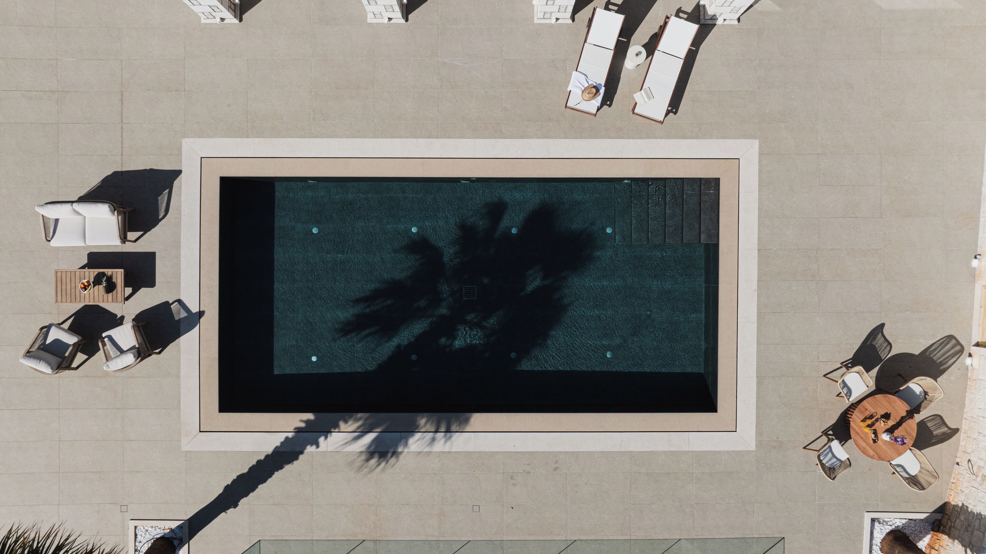 Vue aérienne d’un espace piscine sur le toit, avec des chaises longues, une table et un palmier.