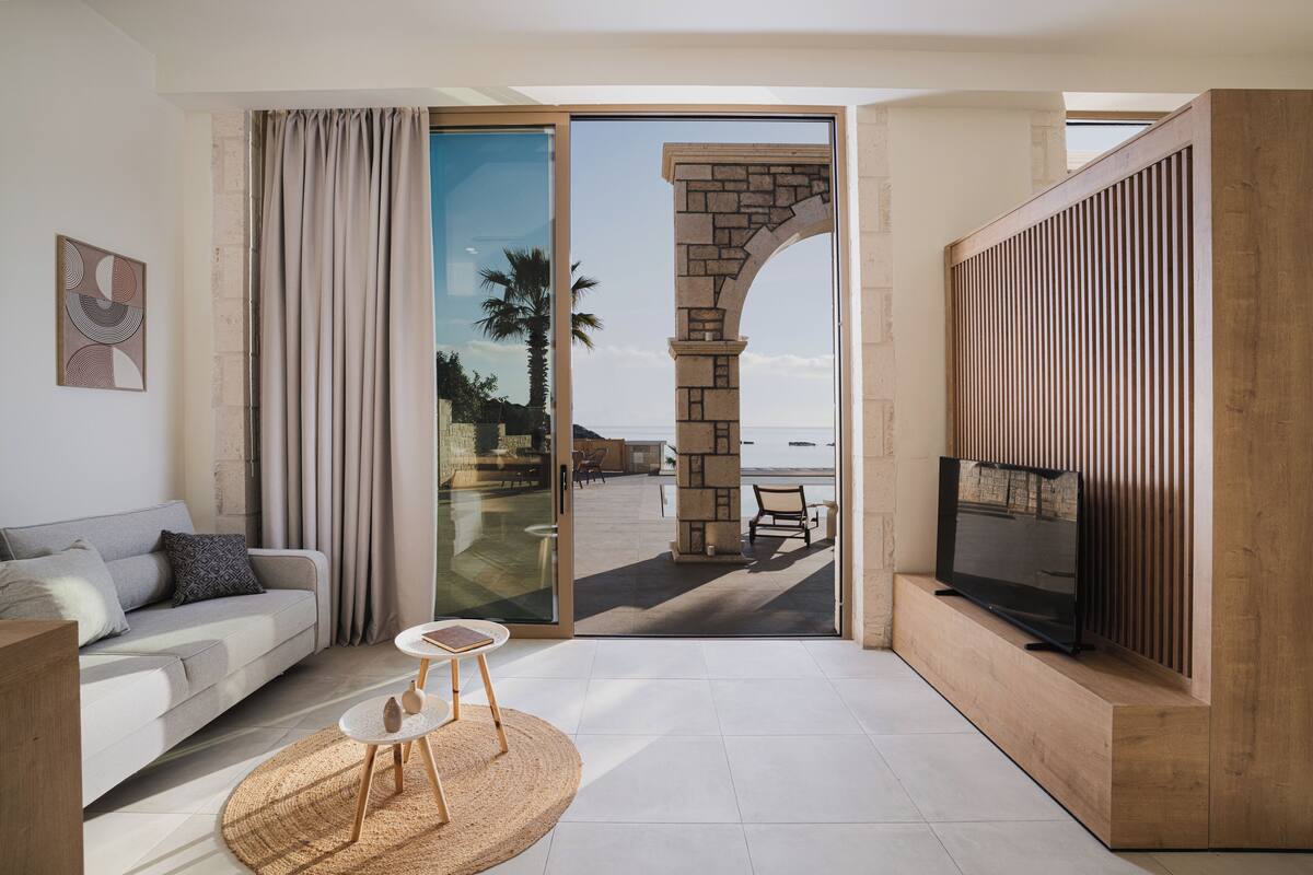 A modern living room with a sofa, TV, and a view of the beach.