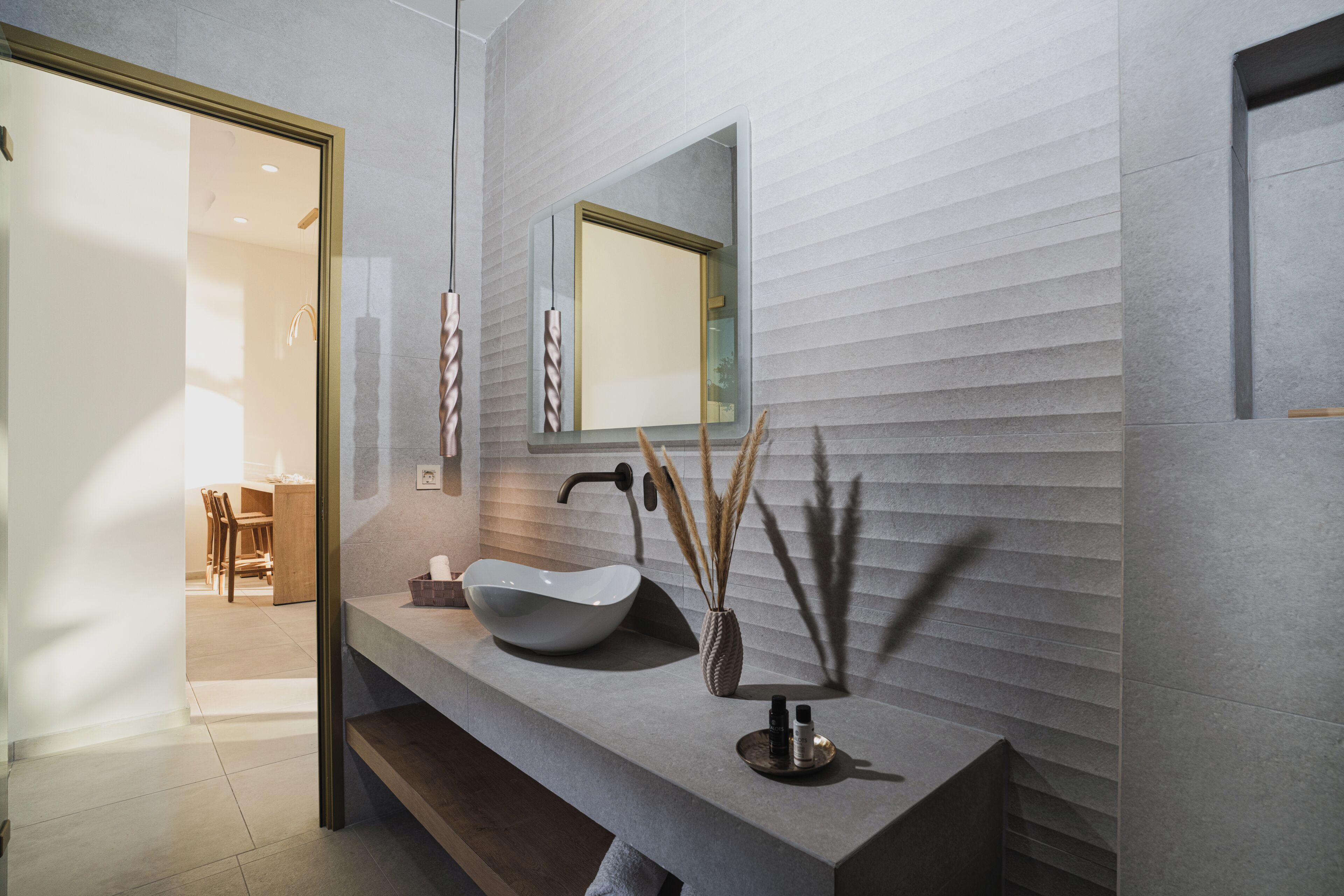 Un baño moderno con un lavamanos de pedestal grande, un espejo y un florero con cañas decorativas.