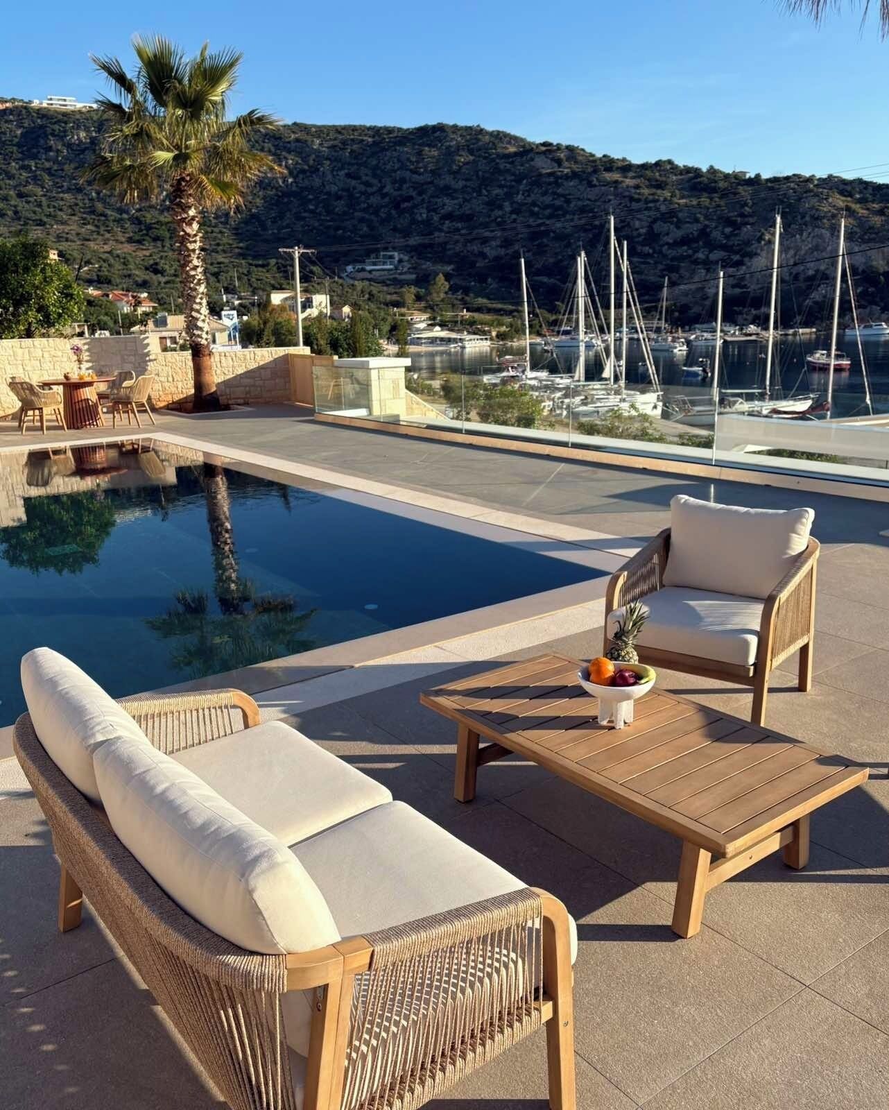 A poolside area with lounge chairs, a table with fruit, and a view of a marina and hills.