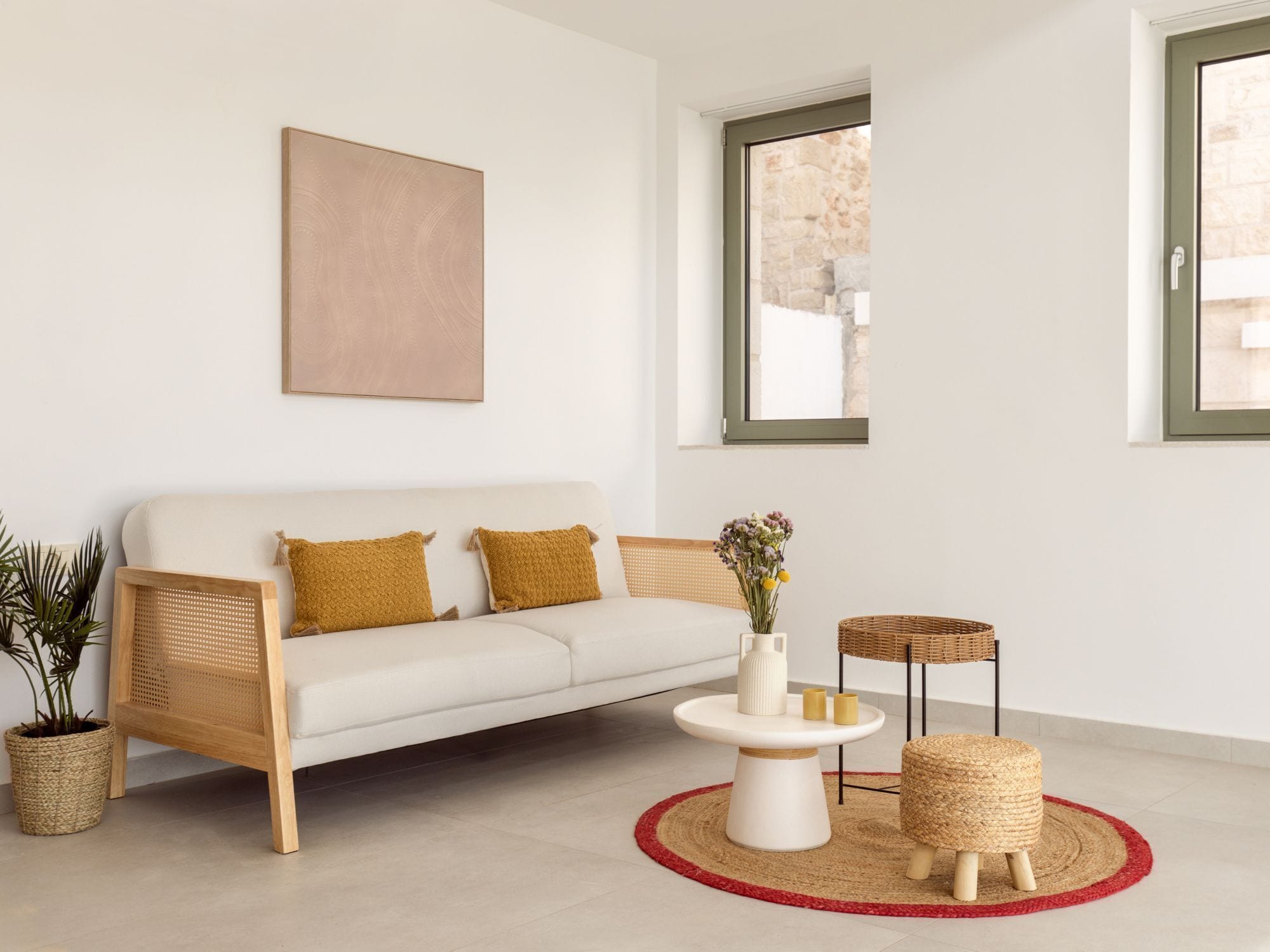 Una sala de estar moderna con un sofá blanco, una mesa redonda de centro y una mesita auxiliar de mimbre.