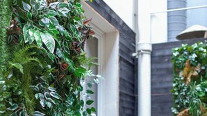 A modern building with a vertical garden on the exterior wall, a small potted plant on the ground, and a metal structure in the background. - Hotel Tinah: Elegance and Comfort Near the Champs-elysees (Paris)