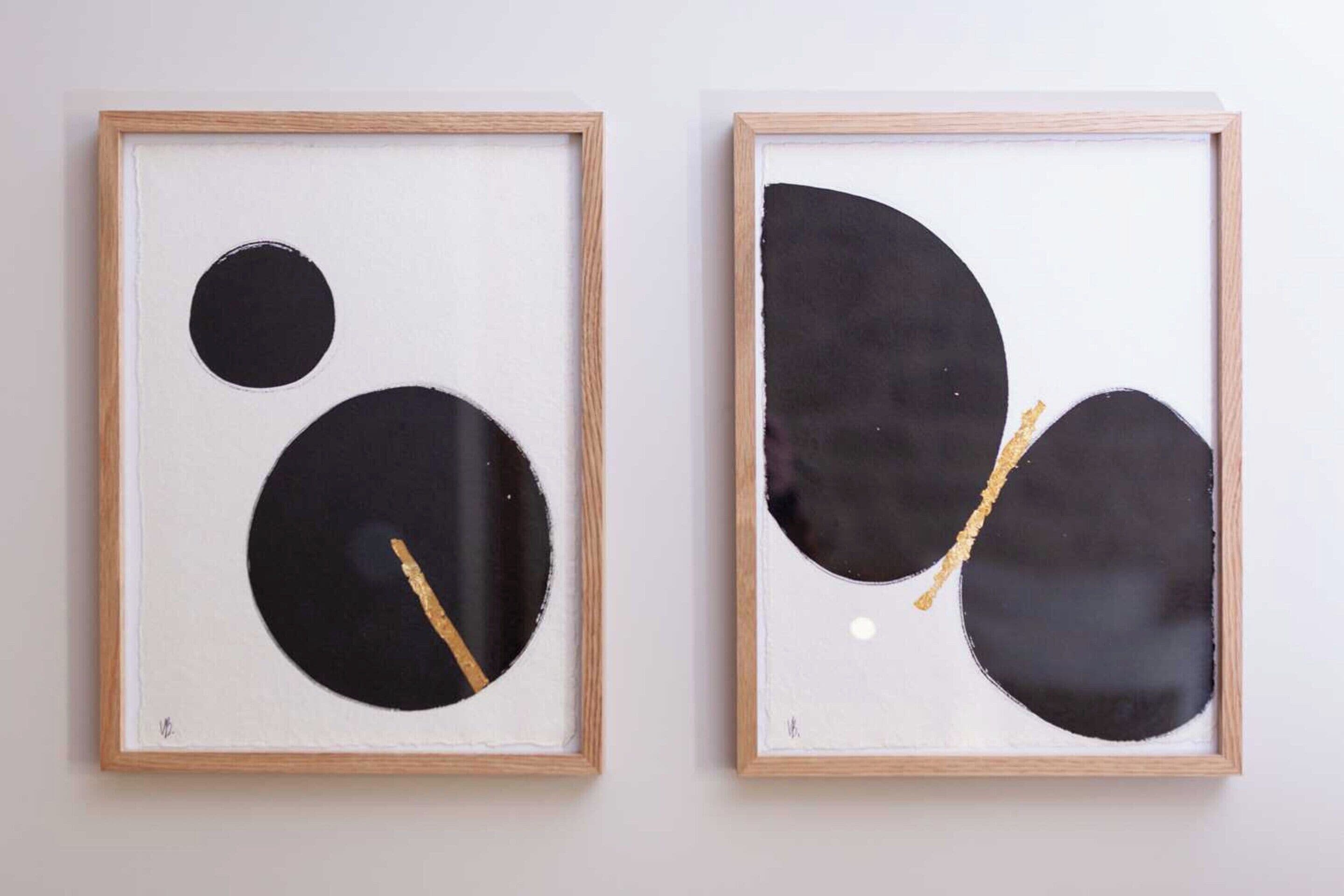 Duas pinturas abstratas emolduradas com molduras de madeira sobre uma parede lisa.