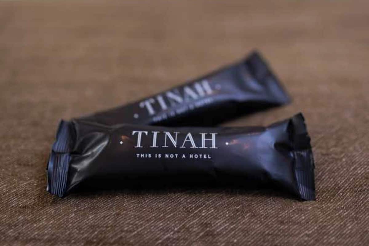 Zwei schwarze 'TINAH'-Packungen auf einer braunen Oberfläche, unscharfer Hintergrund.