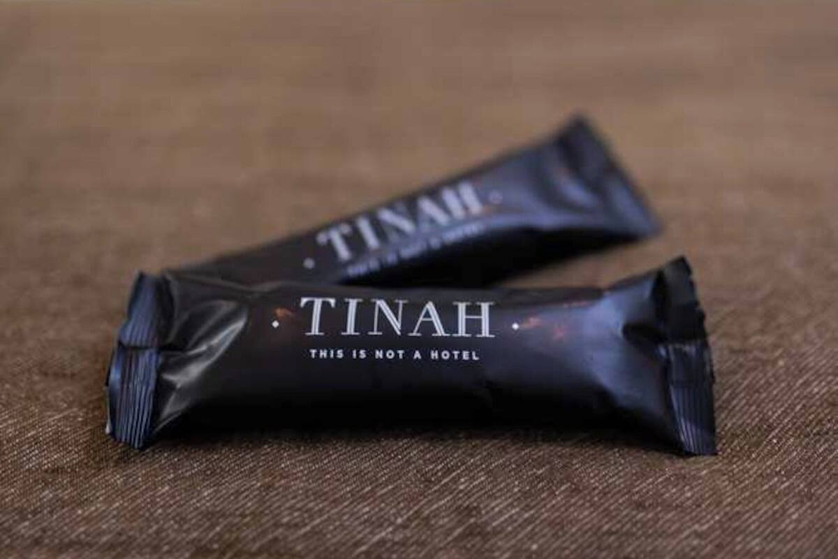 Zwei schwarze Pakete mit dem Aufdruck "TINAH" auf einer strukturierten Oberfläche, unscharfer Hintergrund.