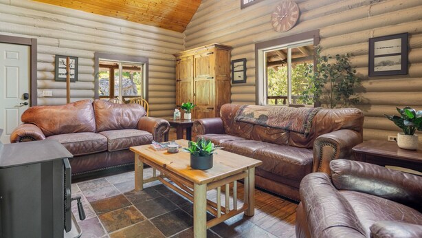 A log cabin interior with a leather sofa set, a wooden coffee table, and a clock on the wall.