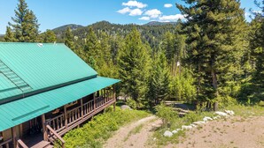 A lodge with a green roof, wooden deck, and a view of a forested mountain range.