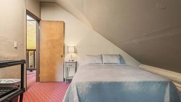 A bedroom with a bed, bedside table, lamp, and a door leading to another room.