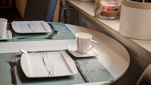 Une table à manger élégamment dressée, avec des assiettes, des couverts et une tasse, une plante en pot et une bougie posée sur un rebord de fenêtre.