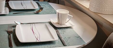 Une table à manger élégamment dressée, avec des assiettes, des couverts et une tasse, une plante en pot et une bougie posée sur un rebord de fenêtre.
