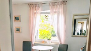 Une pièce avec deux chaises, une petite table, une fenêtre avec des rideaux, un miroir et une plante.