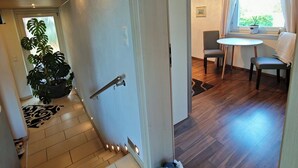 Un couloir avec un escalier menant à une salle à manger, une plante en pot et une petite table avec des chaises.