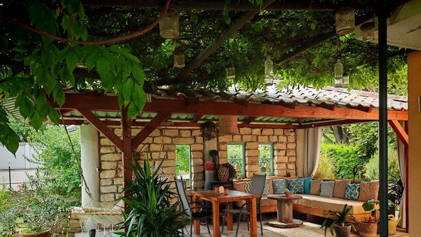 Une terrasse couverte avec un mur en pierre, des meubles en bois et des plantes en pot.