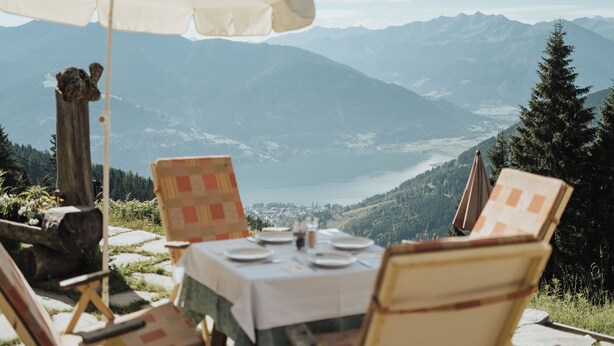 Un espace extérieur aménagé pour prendre les repas, avec une table et des chaises, un poteau en bois, et une vue sur les montagnes et un lac.