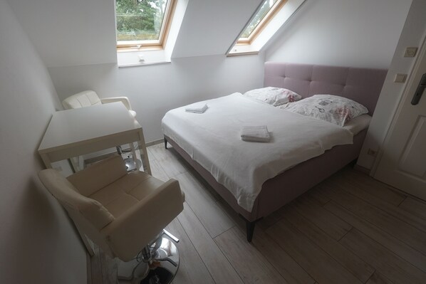 Een slaapkamer met een bed, een bureau en een stoel. Twee ramen zorgen voor natuurlijk licht.