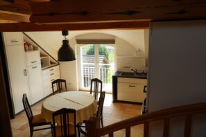 Comedor con mesa y sillas, cocina con pileta y alacenas, y vista a un espacio exterior por una puerta.
