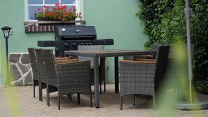 An outdoor patio with wicker furniture, a grill, and a potted plant.